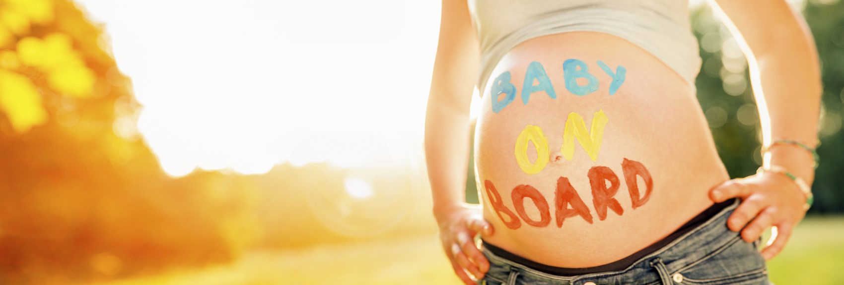 Close-up Of baby On Board Written On Woman's Belly Standing In Garden